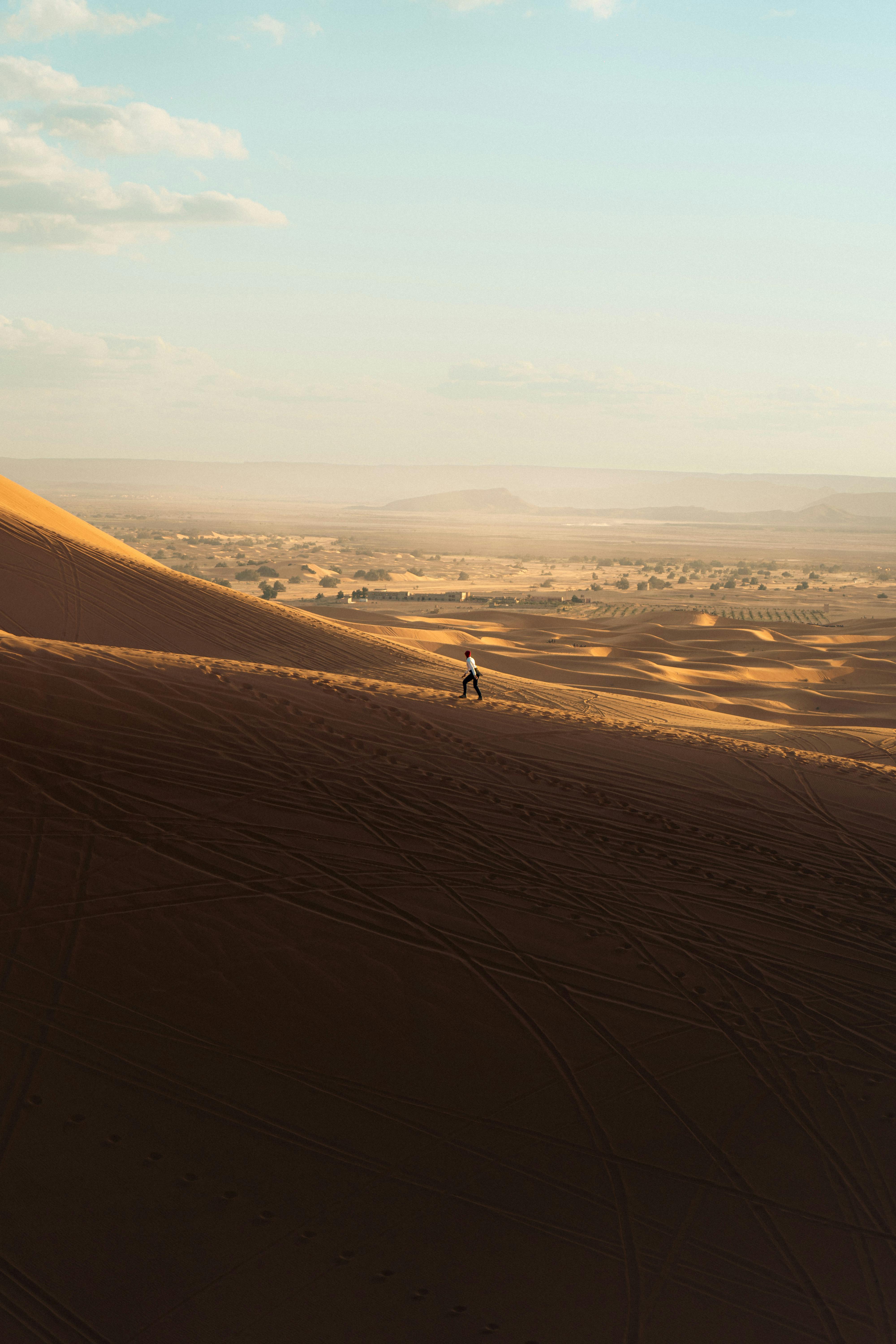 A lone person walks across a sunlit desert dune under a clear blue sky.