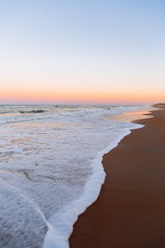 Tranquil ocean waves wash ashore at sunset, capturing a moment of serene beauty at a sandy beach.