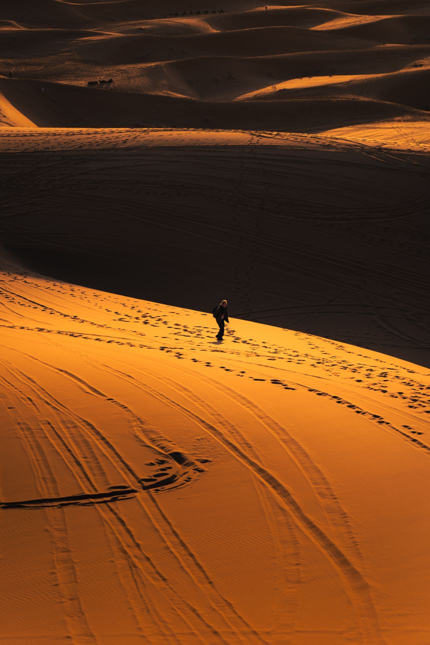 Lone hiker crossing rippled orange sand dunes at sunset, photo by Othmane Ettalbi on Pexels