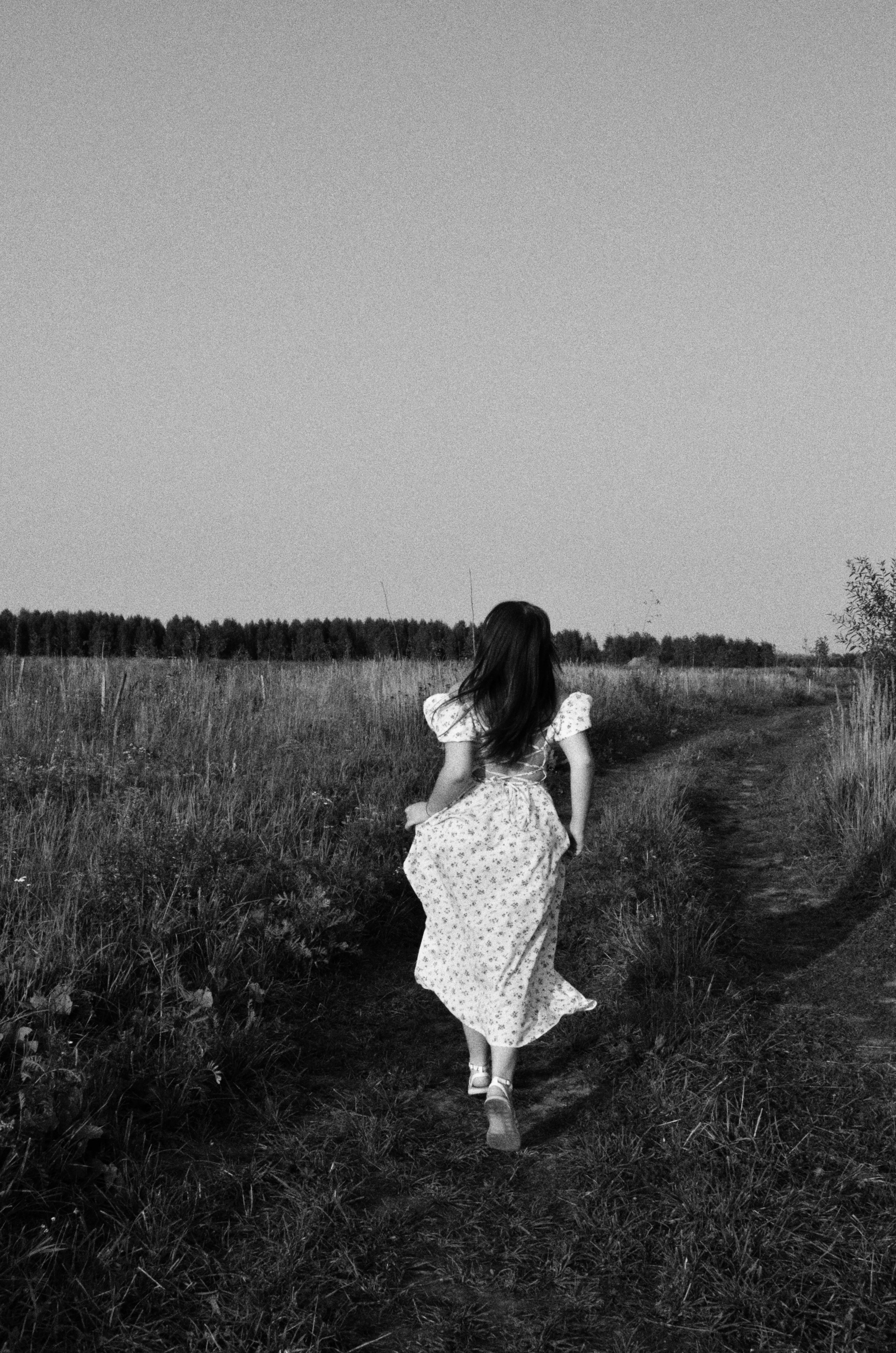 A woman in a flowing dress walks down a rural path in a serene landscape.