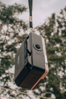 Old black film projector hanging outdoors against a tree backdrop.