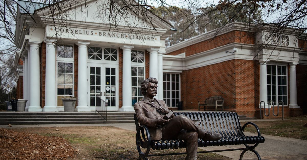 Bronze statue of Mark Twain on a bench by Cornelius Branch Library facade.
