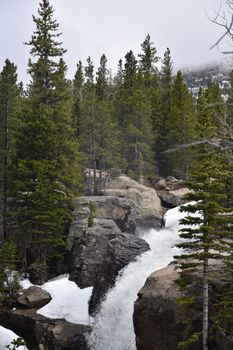 Scenic mountain waterfall flowing through rocks and pines in a tranquil forest setting.