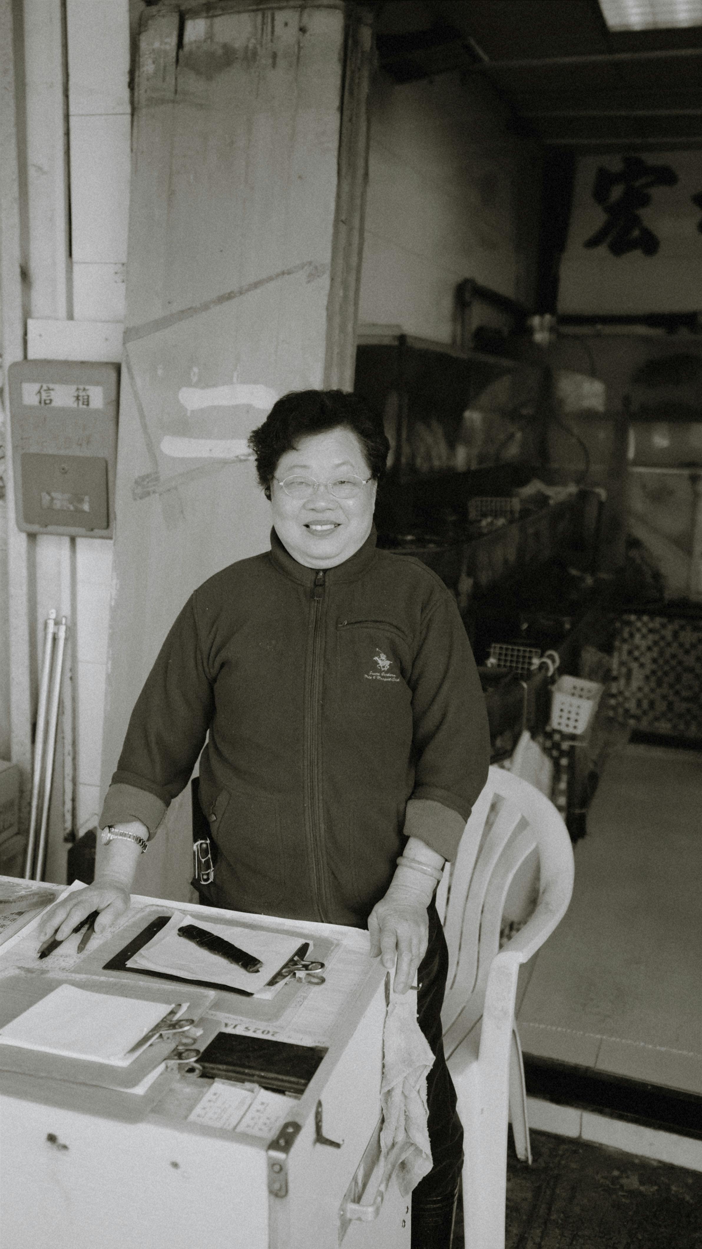 Black and white portrait of a smiling woman inside a market stall.