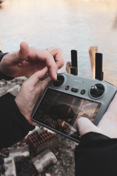 Close-up of hands operating a drone remote controller by a riverside, showcasing technology use outdoors.