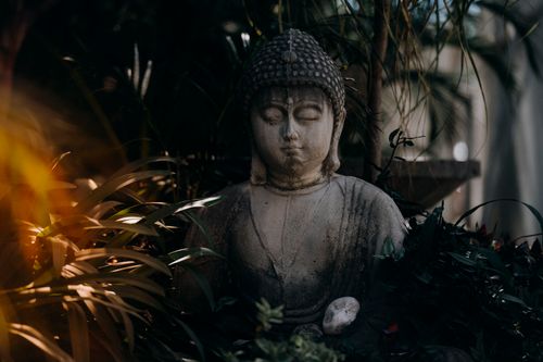 Free A tranquil Buddha statue surrounded by lush garden foliage and natural light. Stock Photo