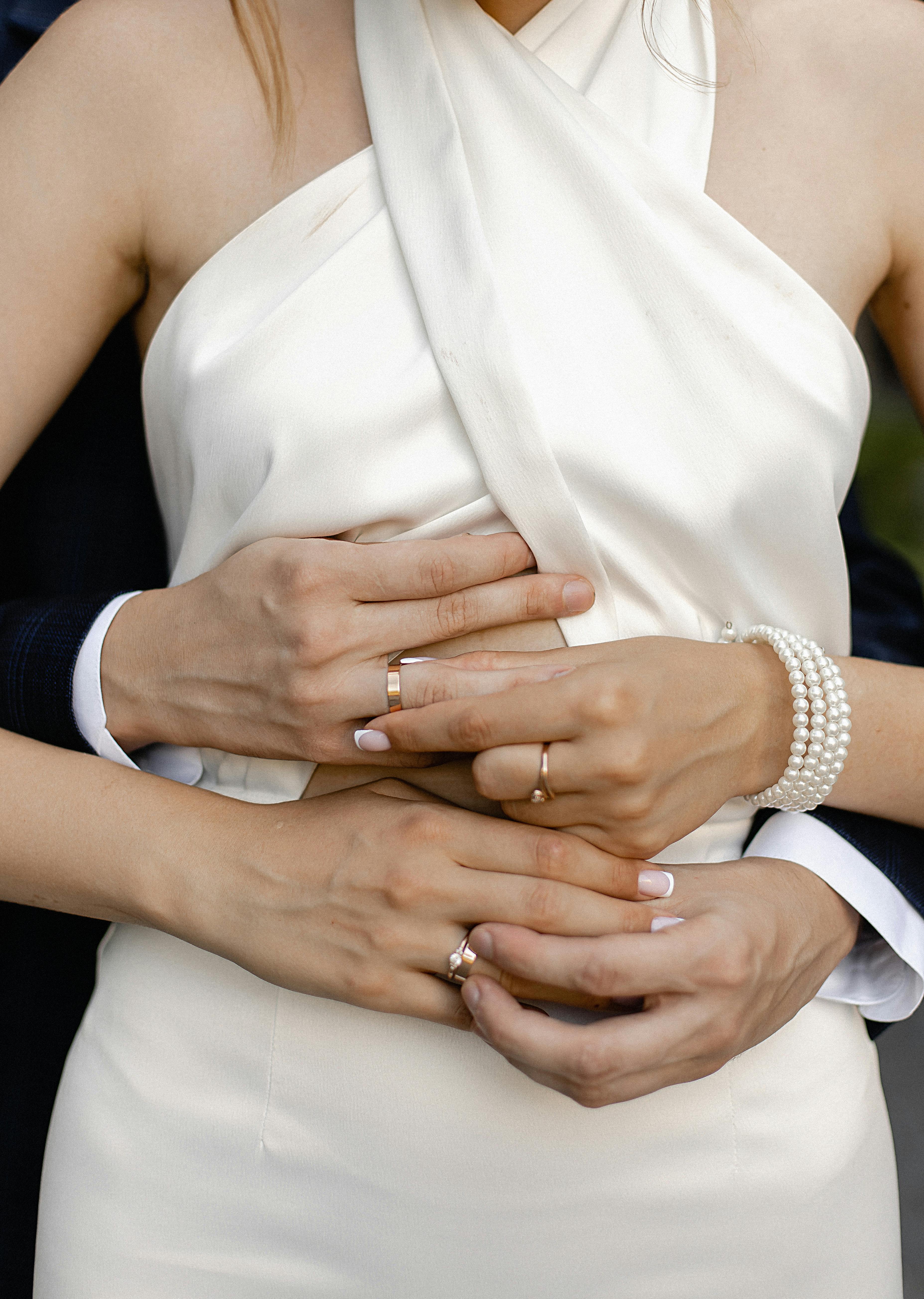 Close-up of newlywed couple's hands showing wedding rings and elegant attire, symbolizing love and commitment.