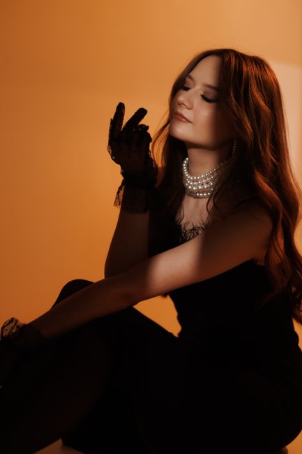 A fashionable woman in elegant attire poses dramatically against a warm background.