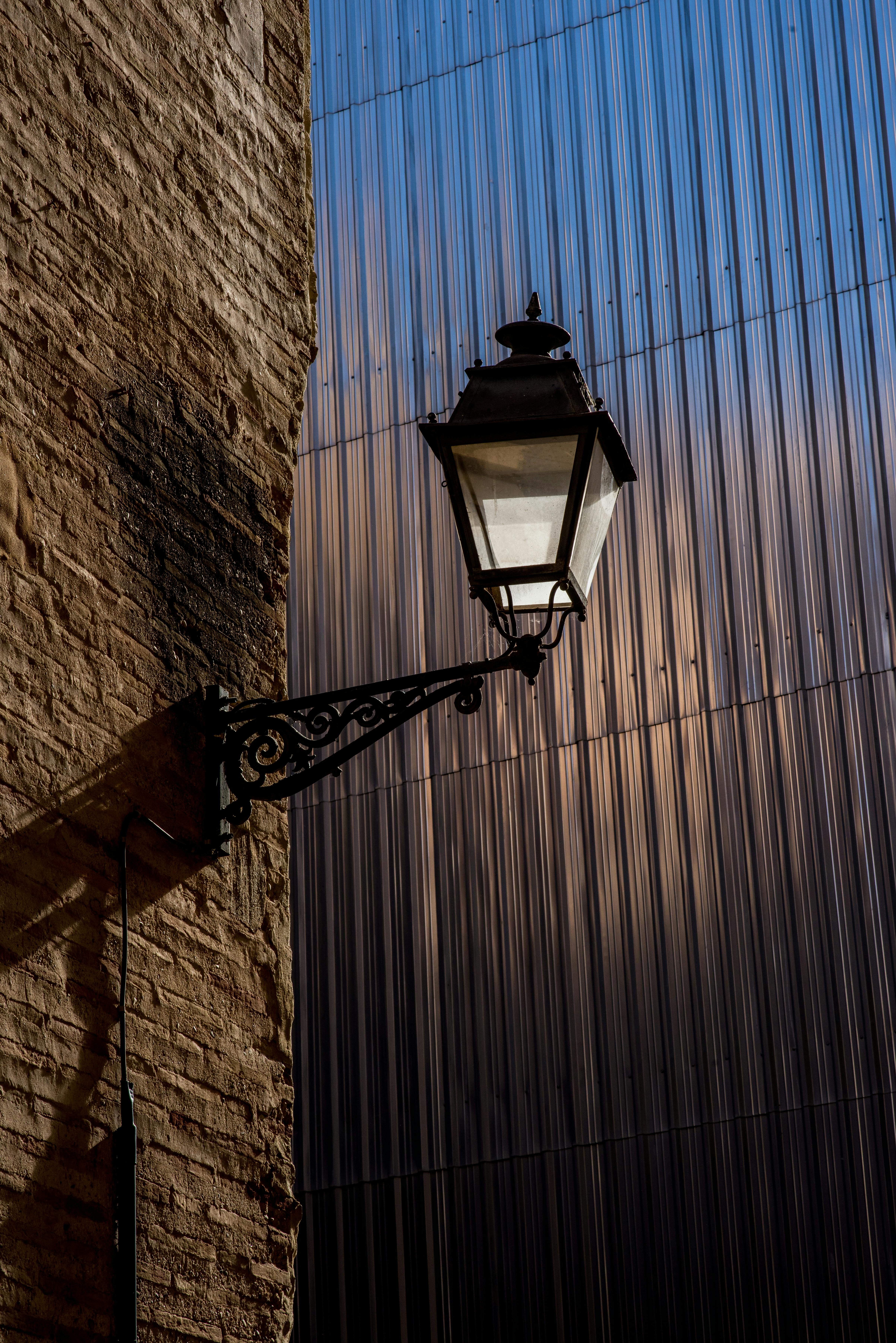 Classic street lamp on rustic wall with modern metal backdrop at dusk.
