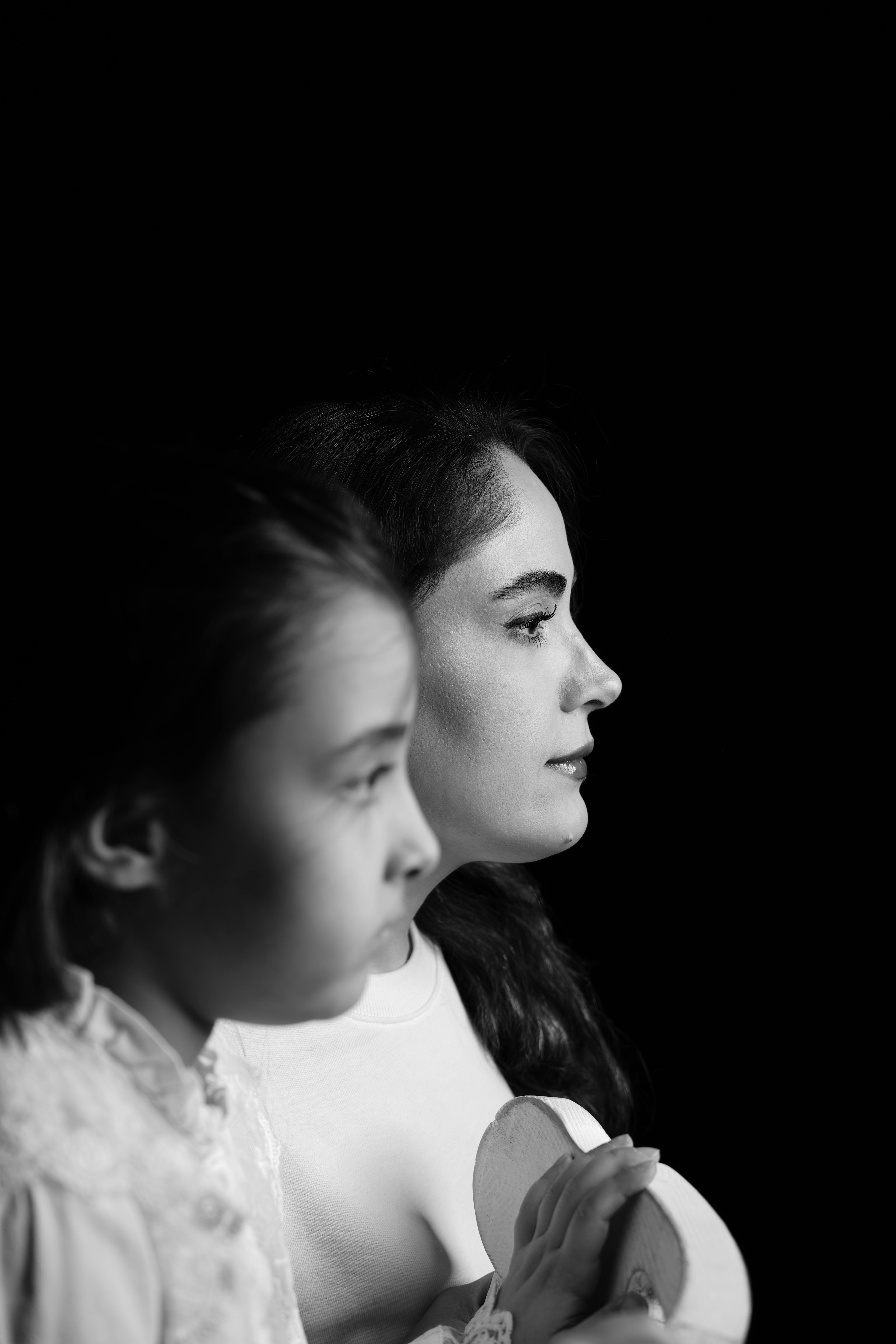 Artistic black and white side portrait of a mother and daughter in focus.