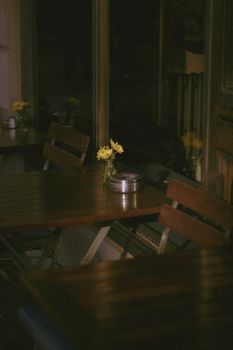A tranquil café setting with wooden tables, chairs, and yellow flowers creating a calm atmosphere.