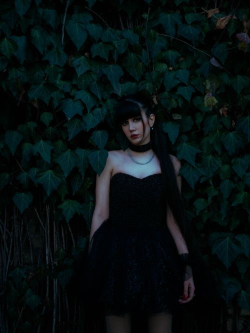 Free Gothic-inspired portrait of a woman standing against a lush ivy backdrop. Stock Photo