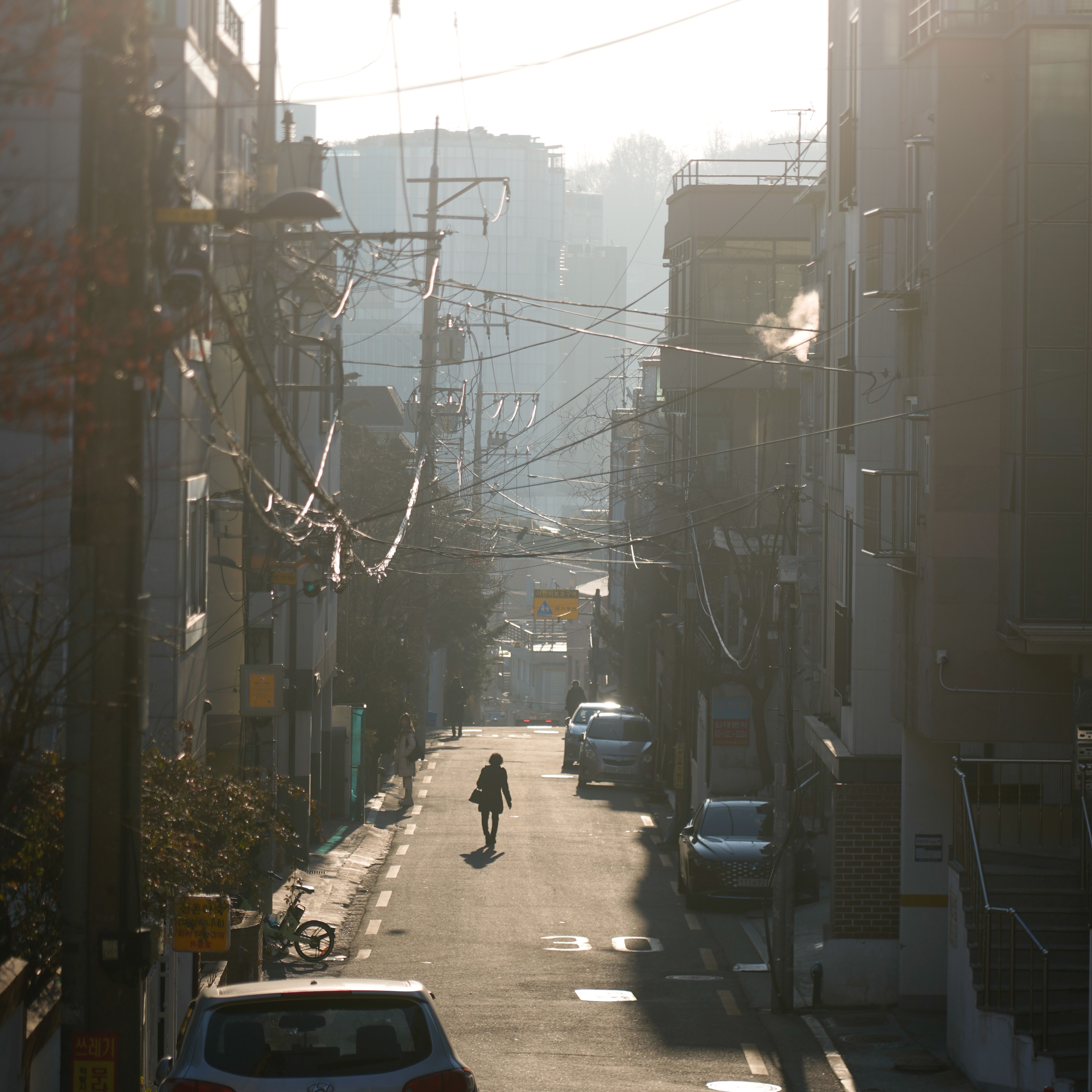 A lone pedestrian walks down a quiet city street lined with buildings at sunrise.