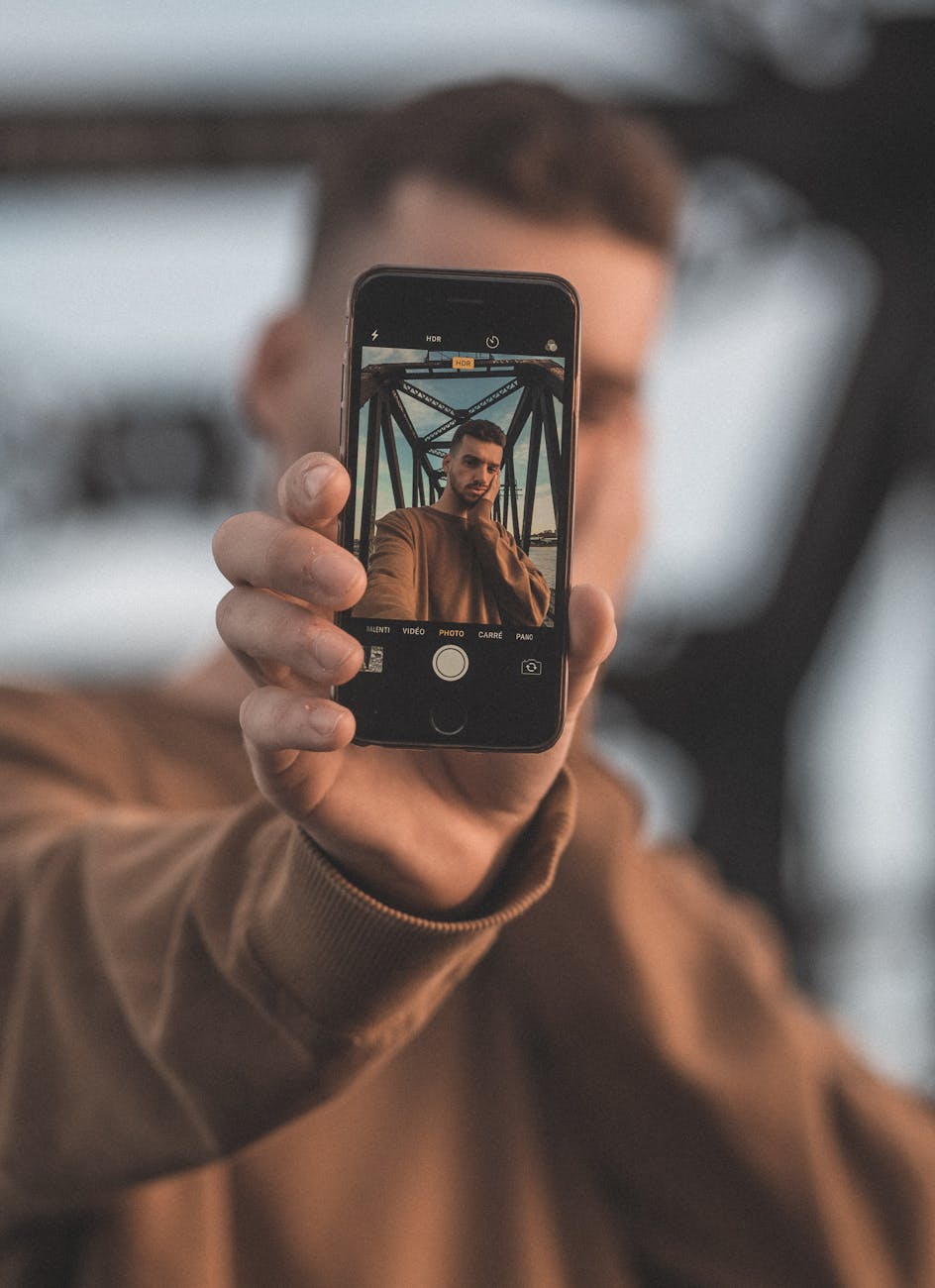 Portrait of a man using a smartphone to take a selfie against an outdoor backdrop.