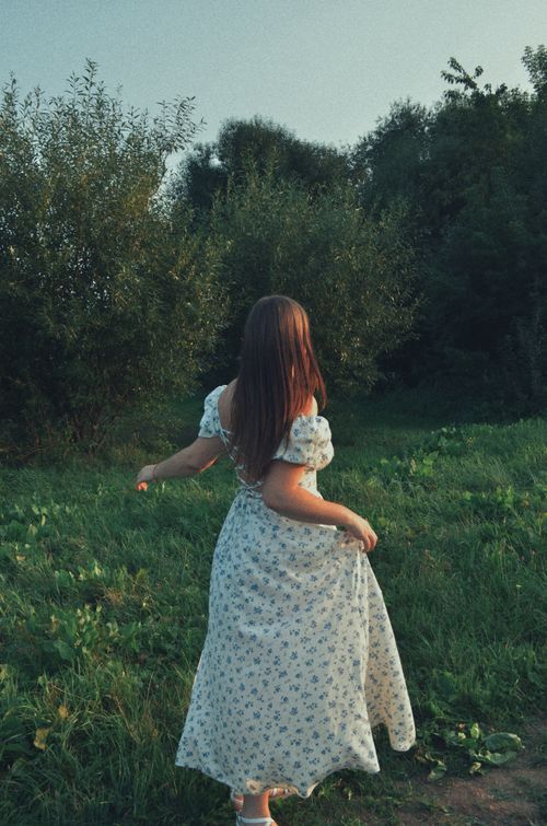 Free A young woman in a vintage floral dress enjoys a serene summer day in a lush green landscape. Stock Photo