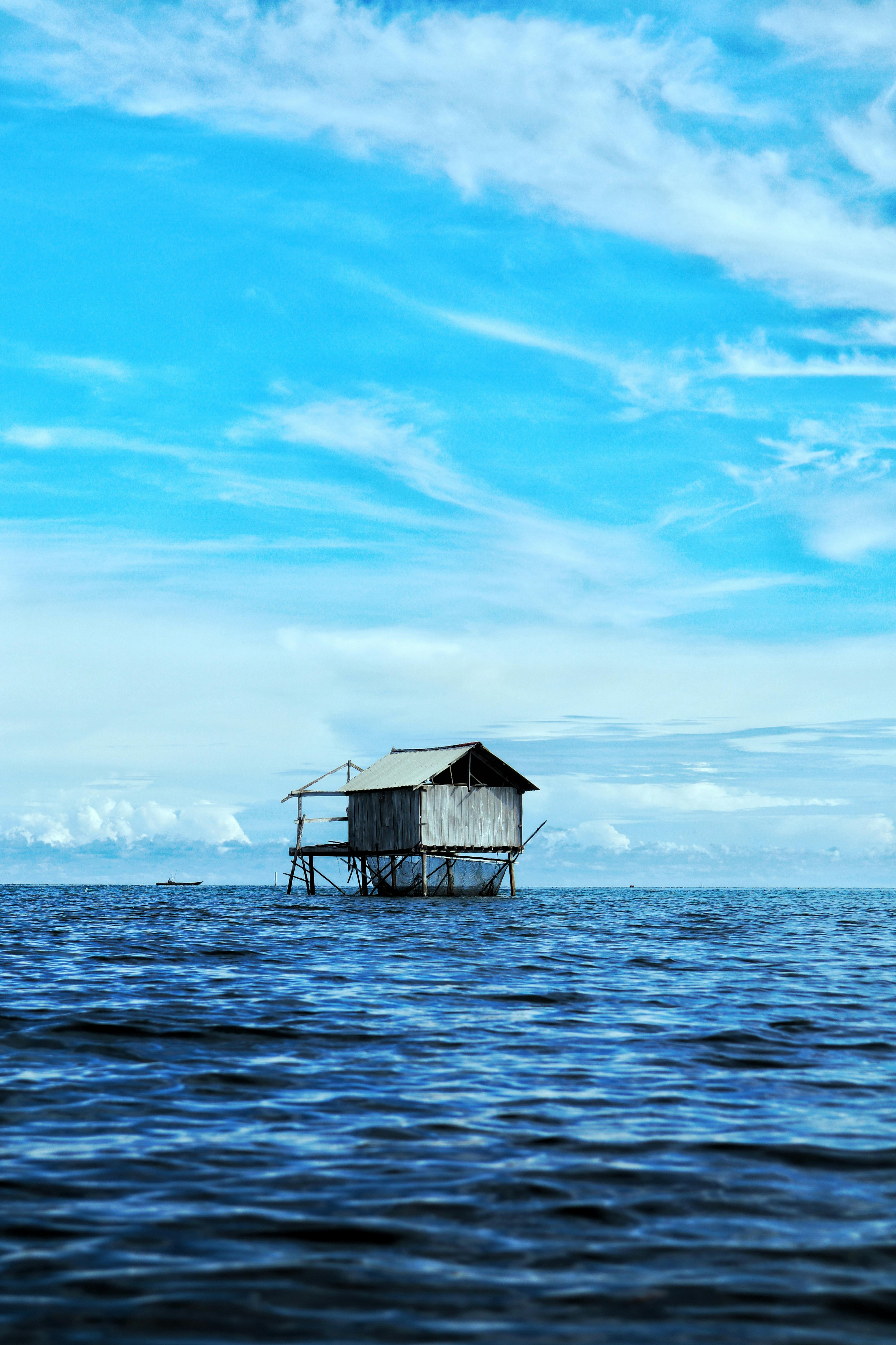 A solitary house on stilts above a calm blue ocean under a clear sky.