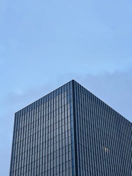 Low-angle view of a modern skyscraper with glass facade under a clear blue sky.