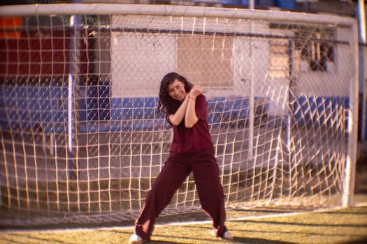Young woman in casual outfit posing cheerfully in front of a soccer goal.