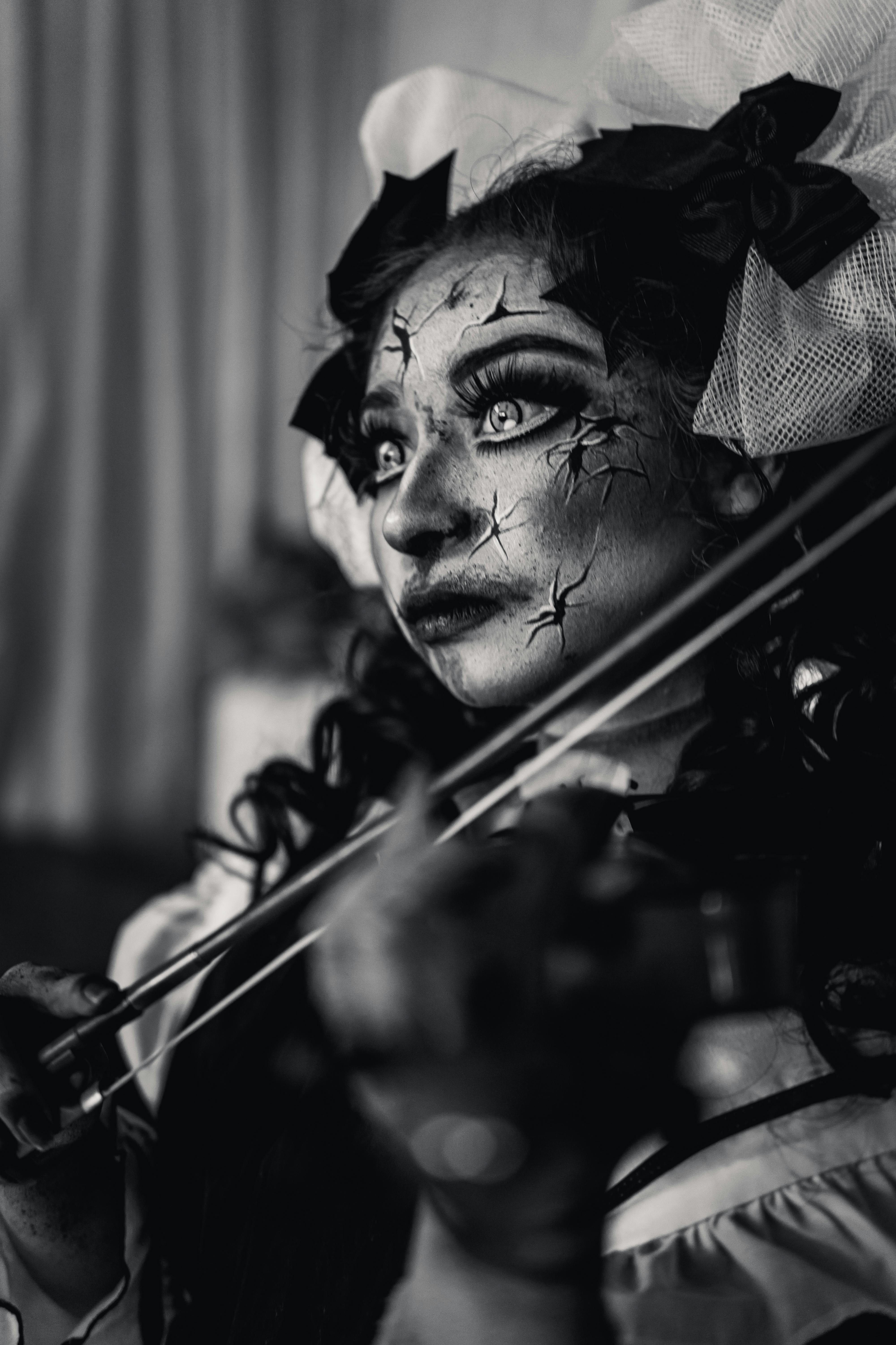 Moody black and white portrait of a costumed violinist with cracked face paint.