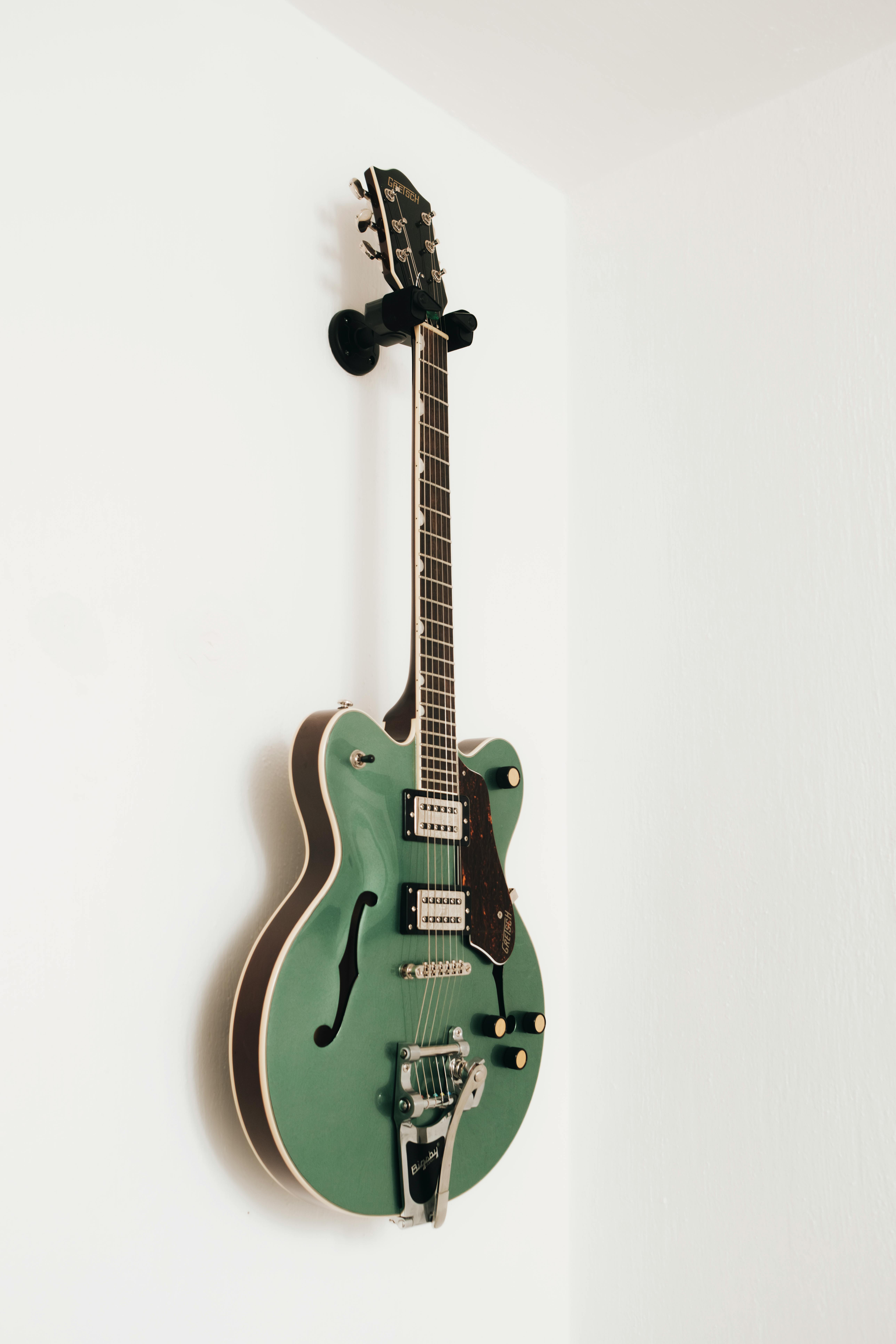 Stylish green electric guitar hanging on a wall in a minimalist setting.