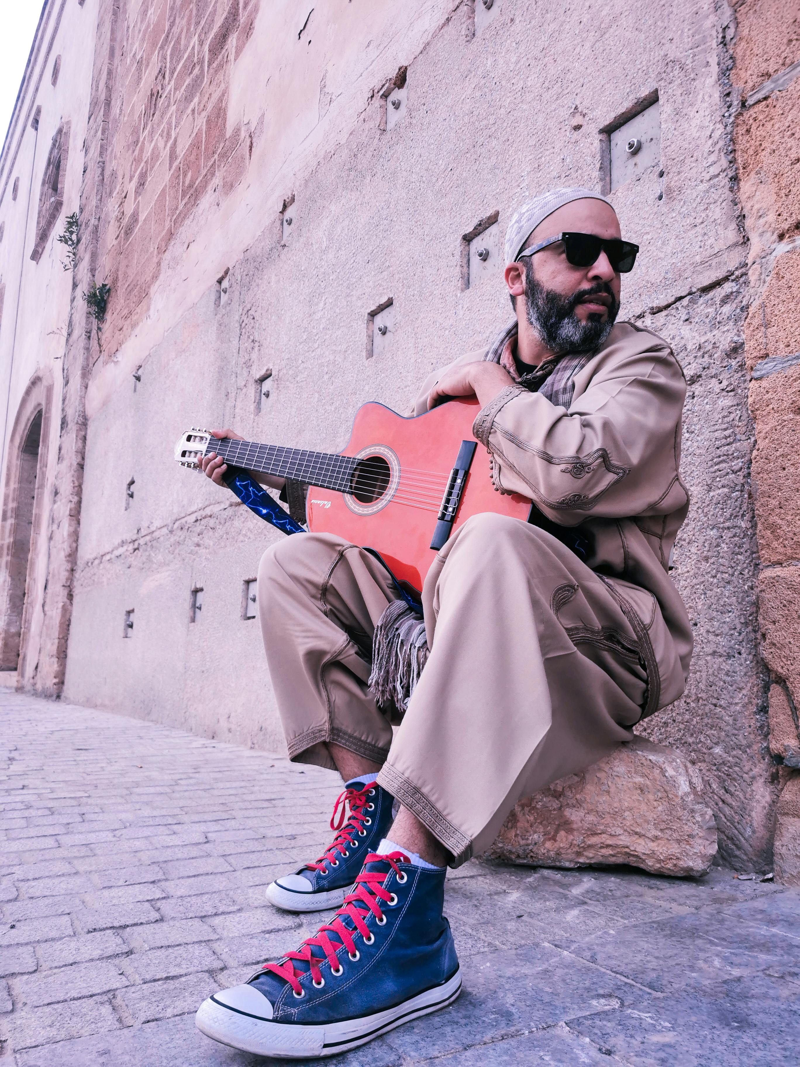 Casual street musician in sunglasses playing guitar against Moroccan architecture.