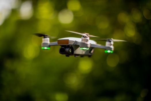 A high-tech drone flying in an outdoor setting with vibrant green bokeh background.