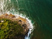 从空中俯瞰，岩石海岸线壮丽非凡，郁郁葱葱的绿色植物与碧绿的海浪一同涌向岸边