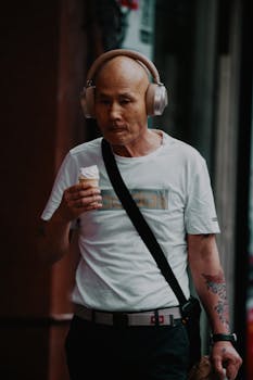 Bald man with headphones eating ice cream outdoors. Street style clothing.