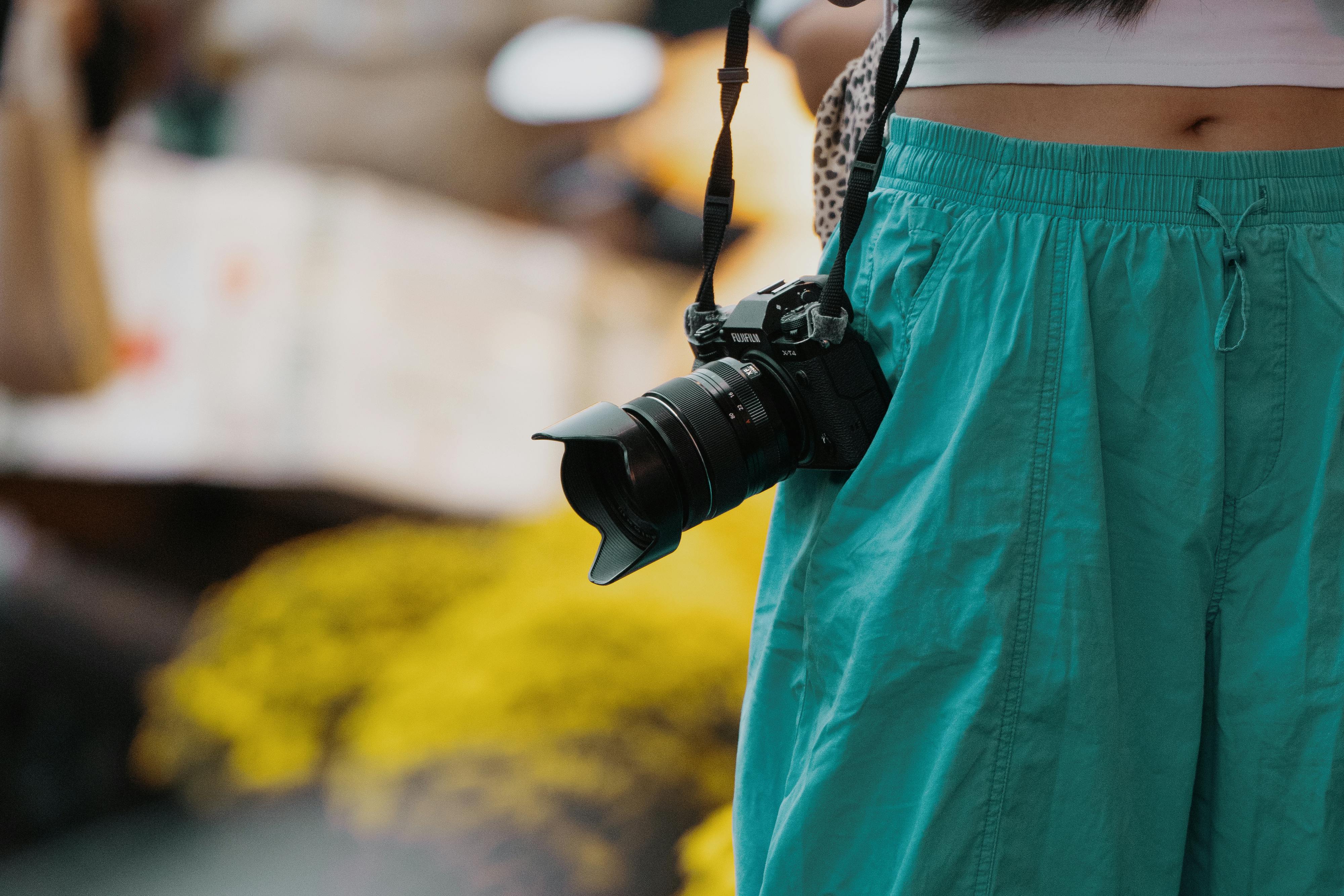 A DSLR camera hangs from the neck of a person standing outdoors in casual clothing.