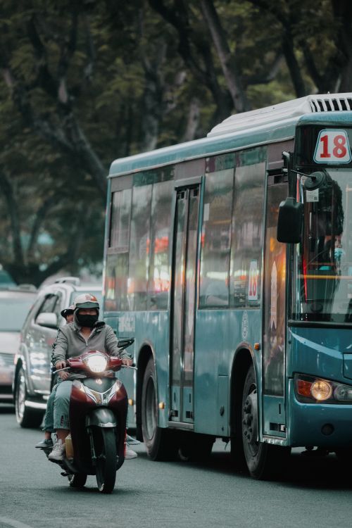 Free A city street scene showcasing a motorcycle and a bus in traffic near lush trees during the day. Stock Photo