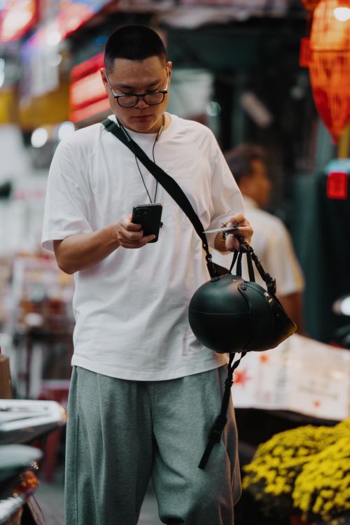 Free Man in casual attire checks smartphone while holding helmet in busy street. Stock Photo