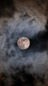 A full moon shining brightly amidst dark, swirling clouds creates a mysterious night sky atmosphere.