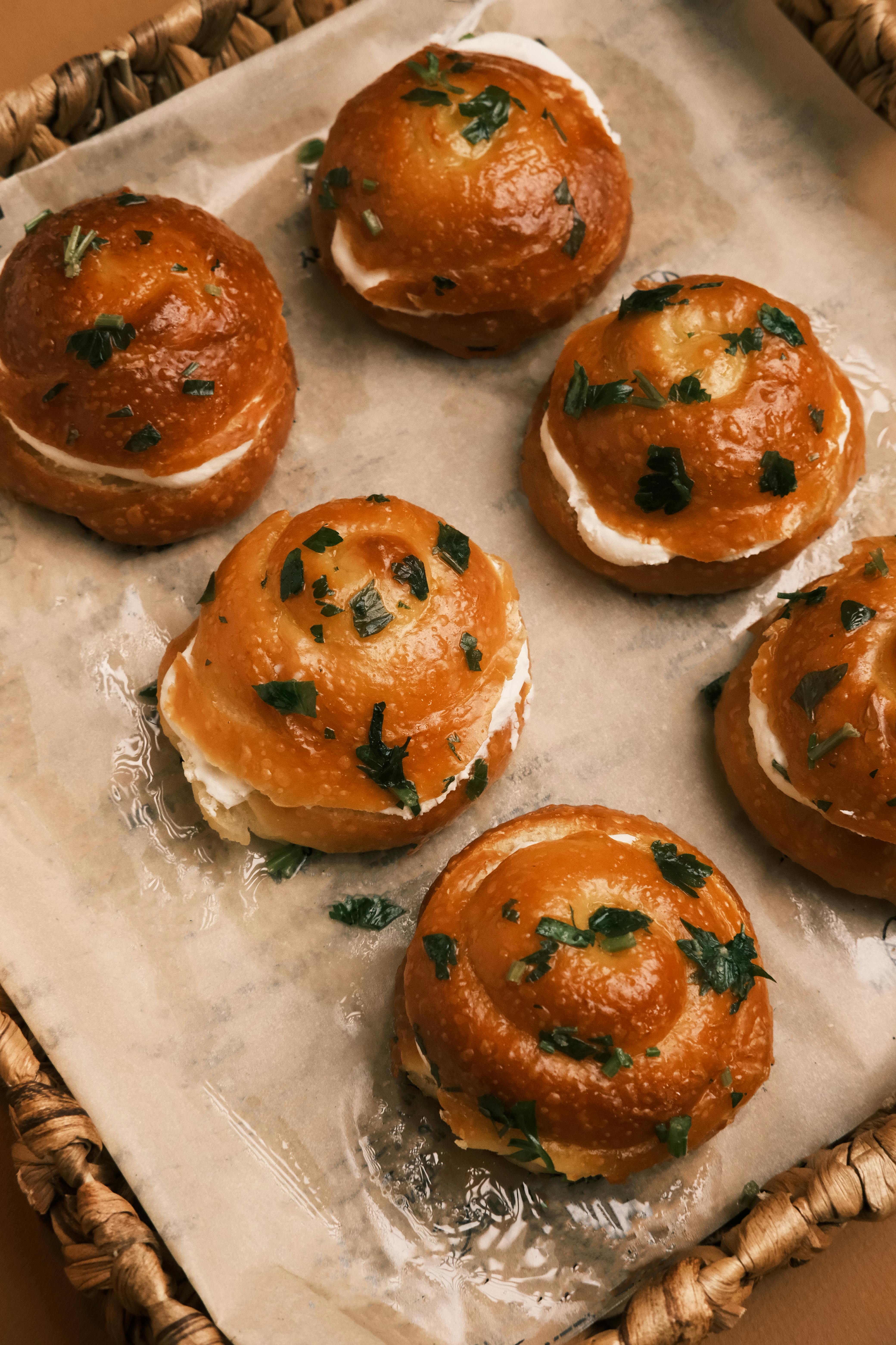Golden brown bread rolls with creamy filling, garnished with fresh parsley, arranged on parchment paper in a woven basket, creating a cozy bakery vibe.