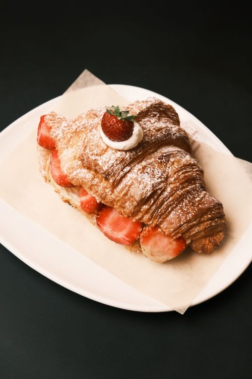 Free Appetizing flaky croissant filled with strawberries and cream on a white plate. Stock Photo