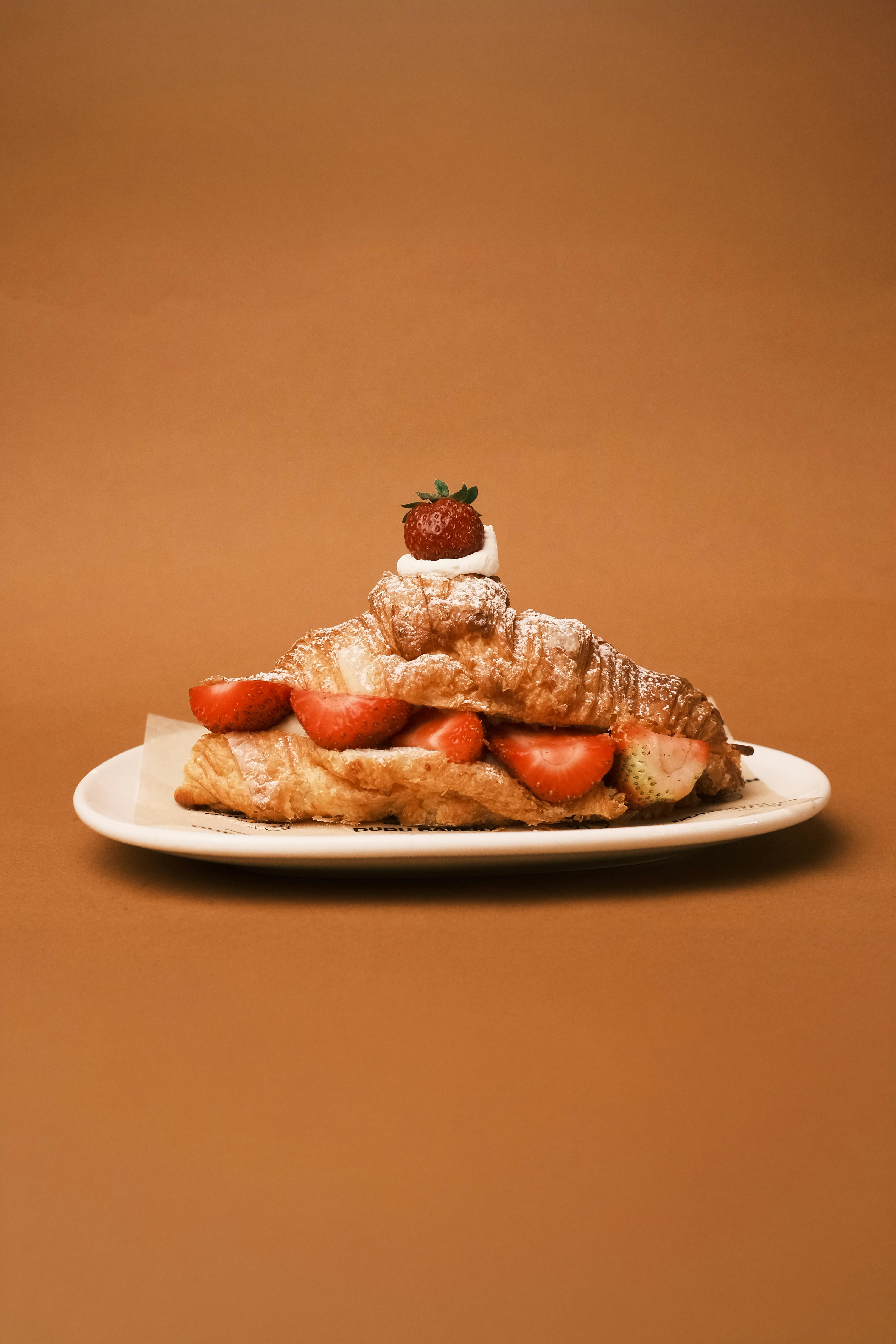 Delicious strawberry-filled croissant on a plate with a warm mocha backdrop, perfect for breakfast or a sweet treat.