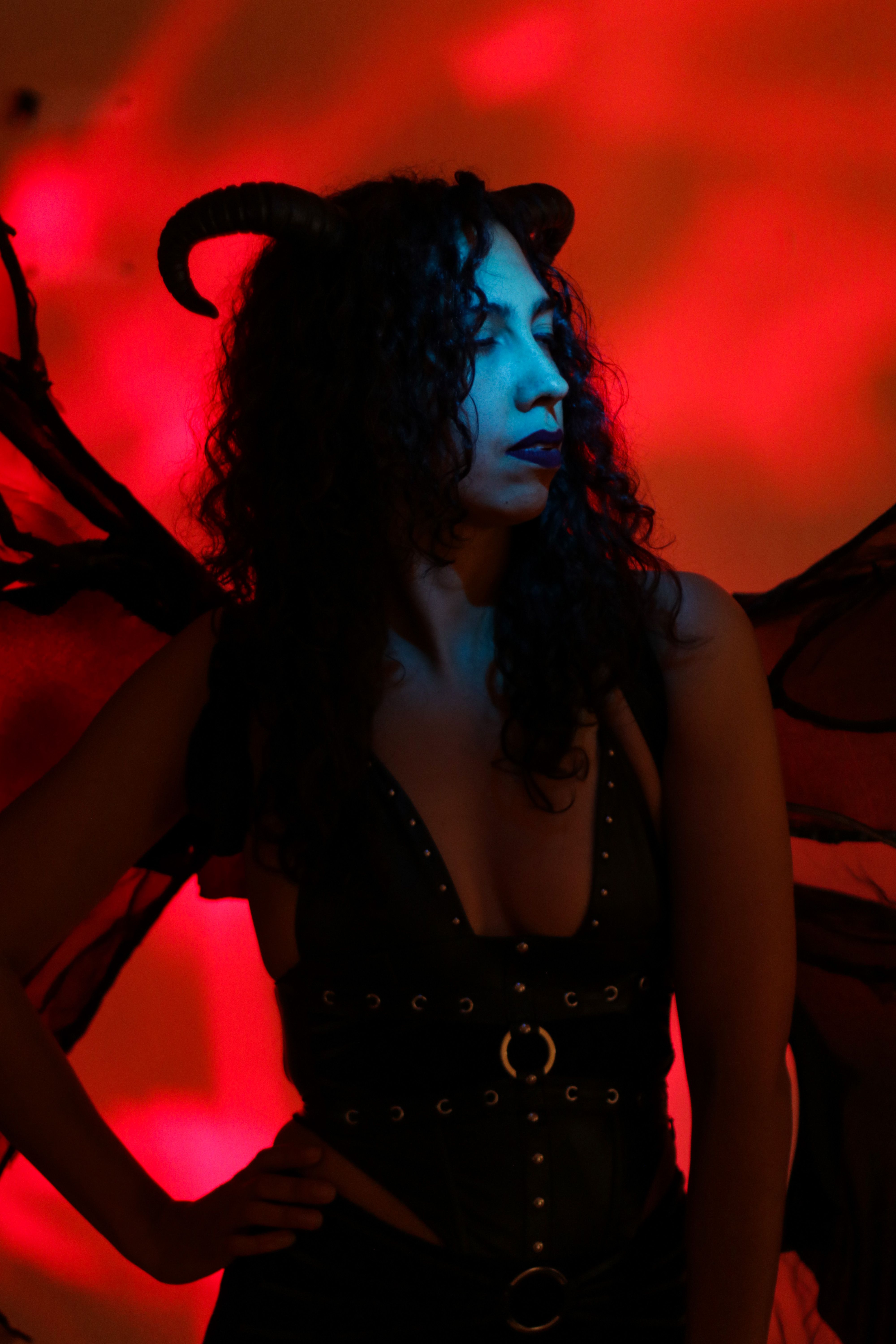 Dark angel figure with horns and wings in dramatic lighting against red background.