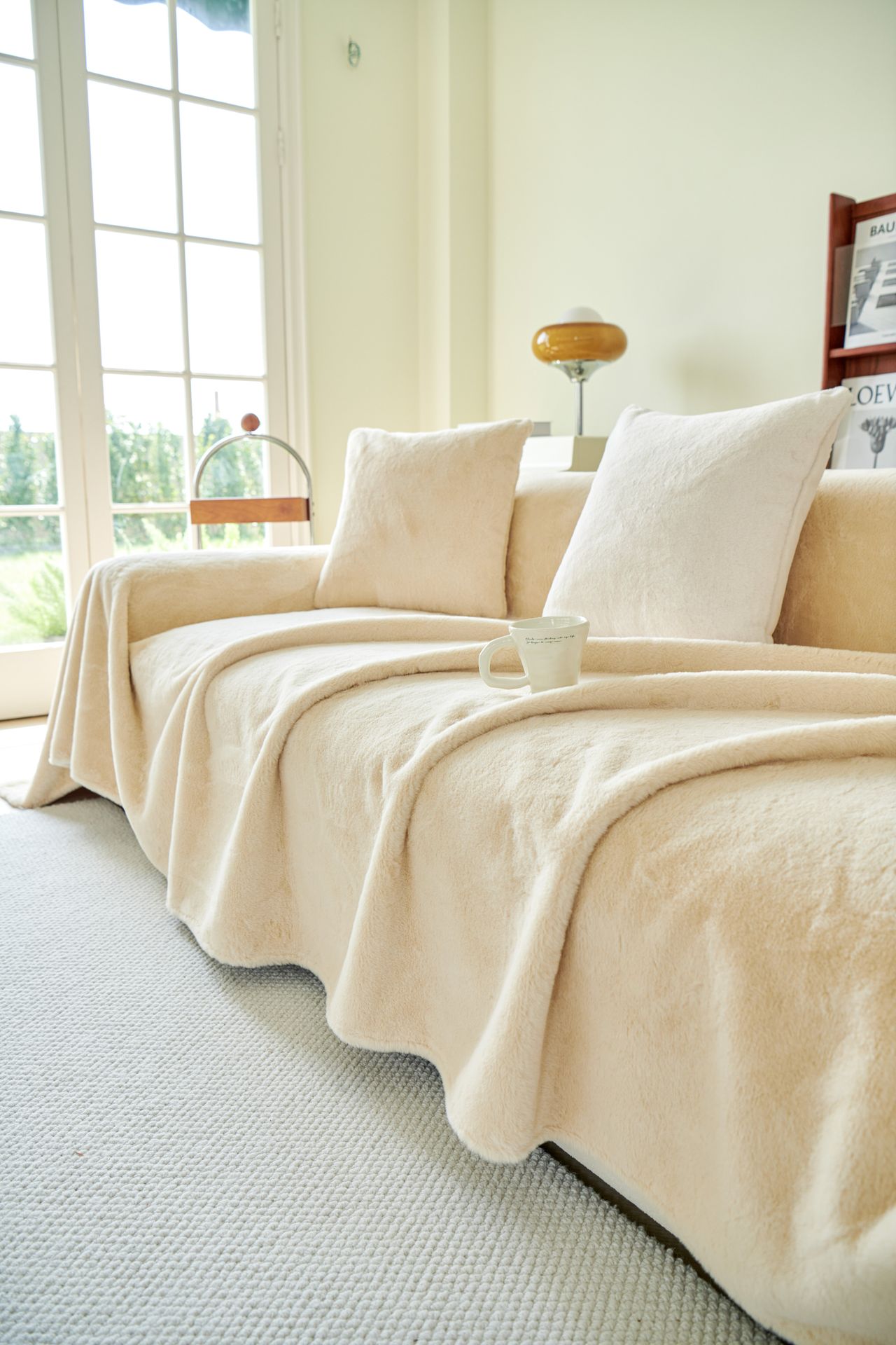 Cream sofa with a soft throw blanket and a cup on the seat