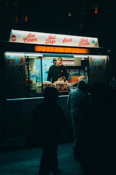 Vibrant street food vendor at night in London, offering ice cream and hot dogs.