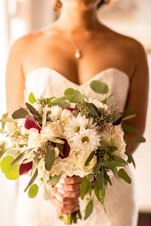 花束の花を保持している白いストラップレスのドレスを着ている女性