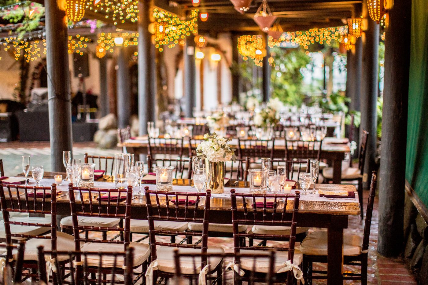 Candlelit long tables under a fairy-lit courtyard colonnade — representative image