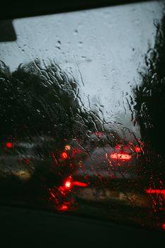 Traffic captured through a car window covered in rain droplets, creating a moody urban scene.