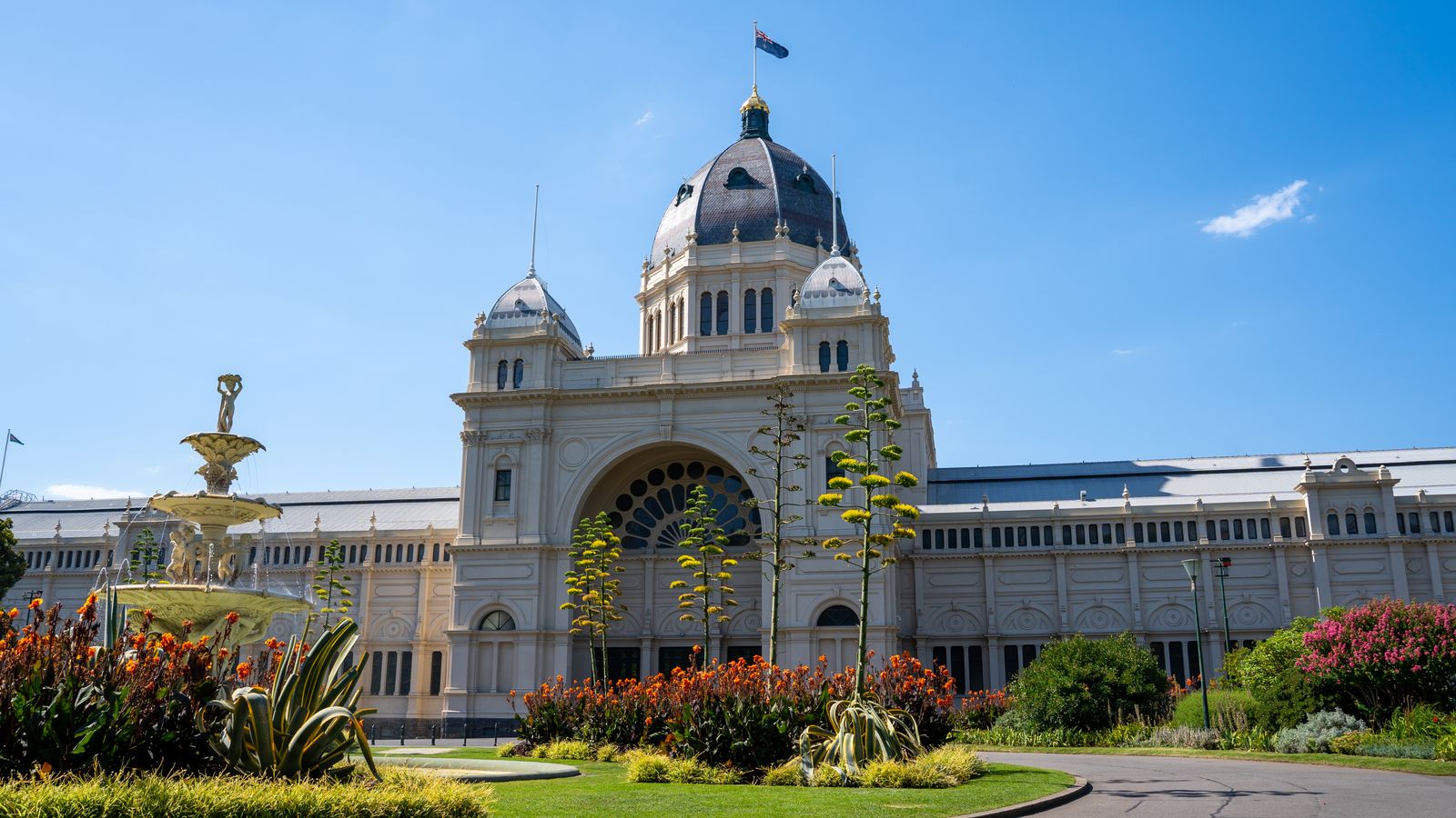 The historic Royal Exhibition Building in Melbourne with vibrant gardens and a clear blue sky.