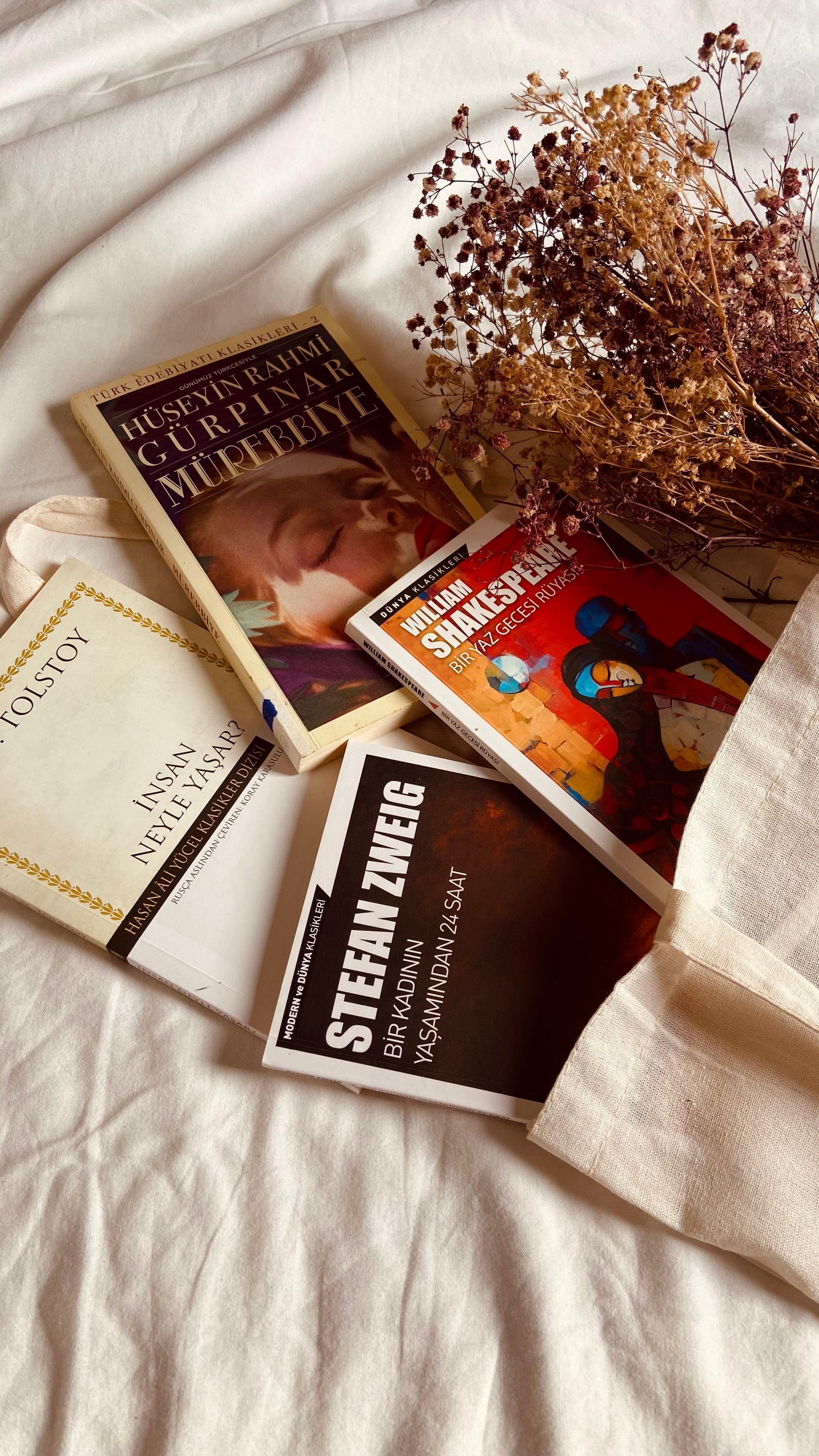 Aesthetic still life with classic books and dried flowers on fabric, creating a cozy literary atmosphere.