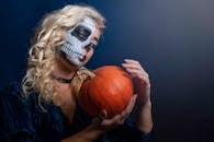 一个画着骷髅脸的女人拿着南瓜，捕捉了万圣节的怪异本质