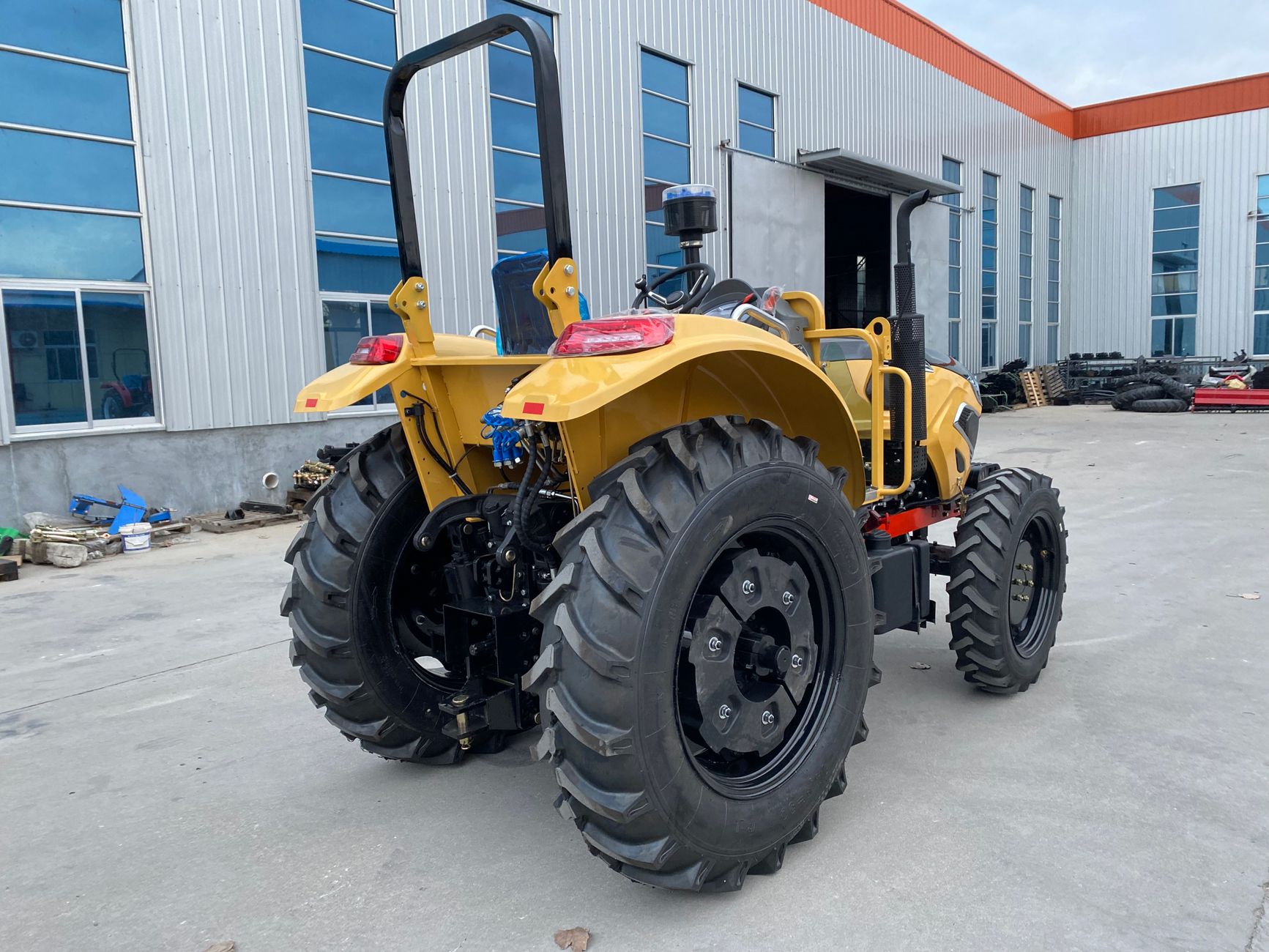 Yellow tractor parked outdoors near a modern industrial building with blue windows.