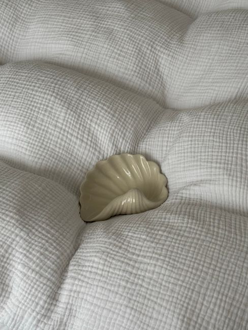 A serene shell-shaped dish rests on soft white bedding, evoking calmness.