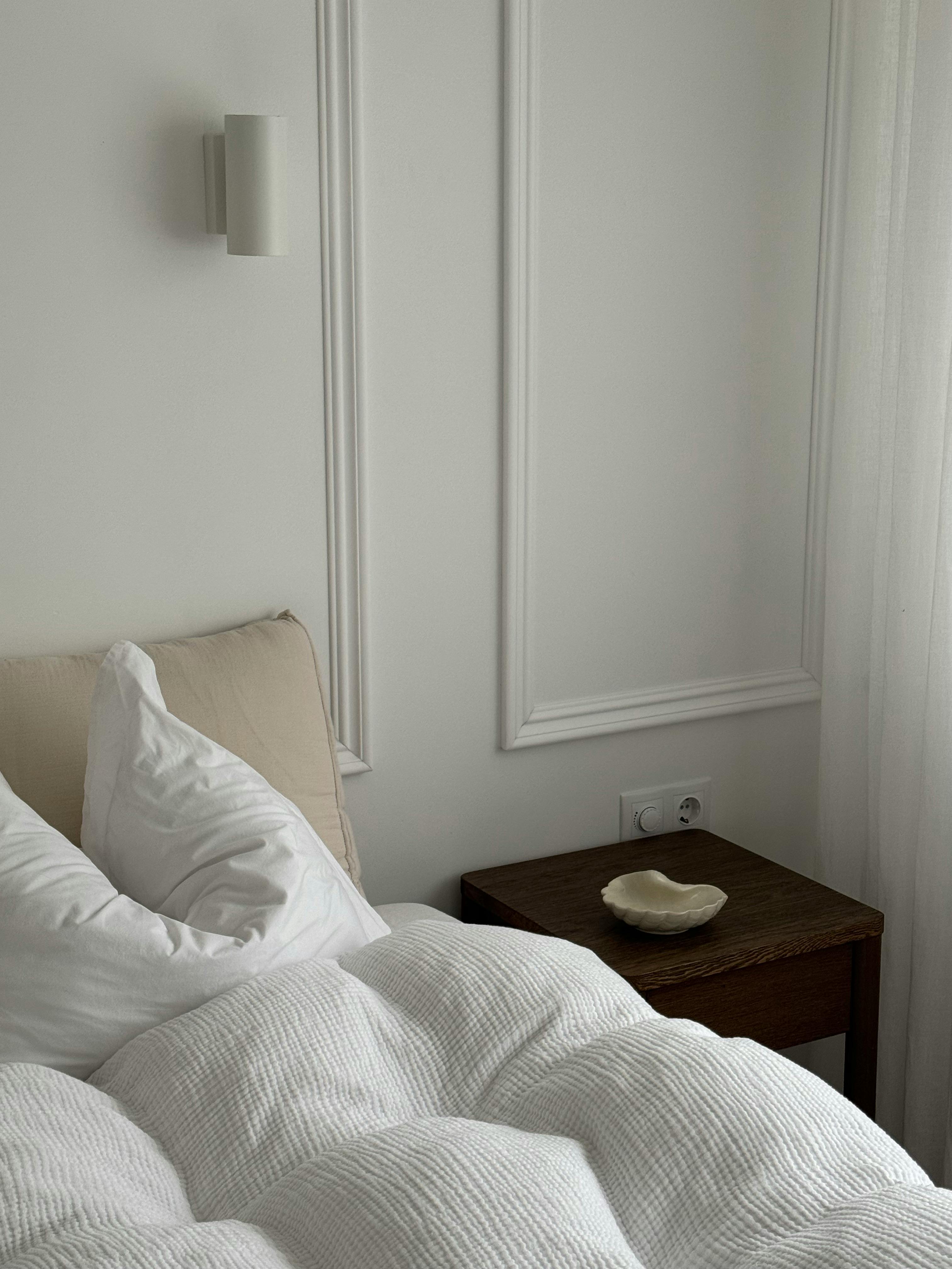A serene minimalist bedroom featuring white bedding and natural light.