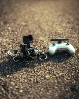 Close-up of a compact drone with a camera and controller on an asphalt surface, ideal for tech and travel imagery.