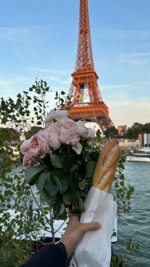 Free Bouquet and baguette held before the Eiffel Tower in Paris, embodying French charm. Stock Photo