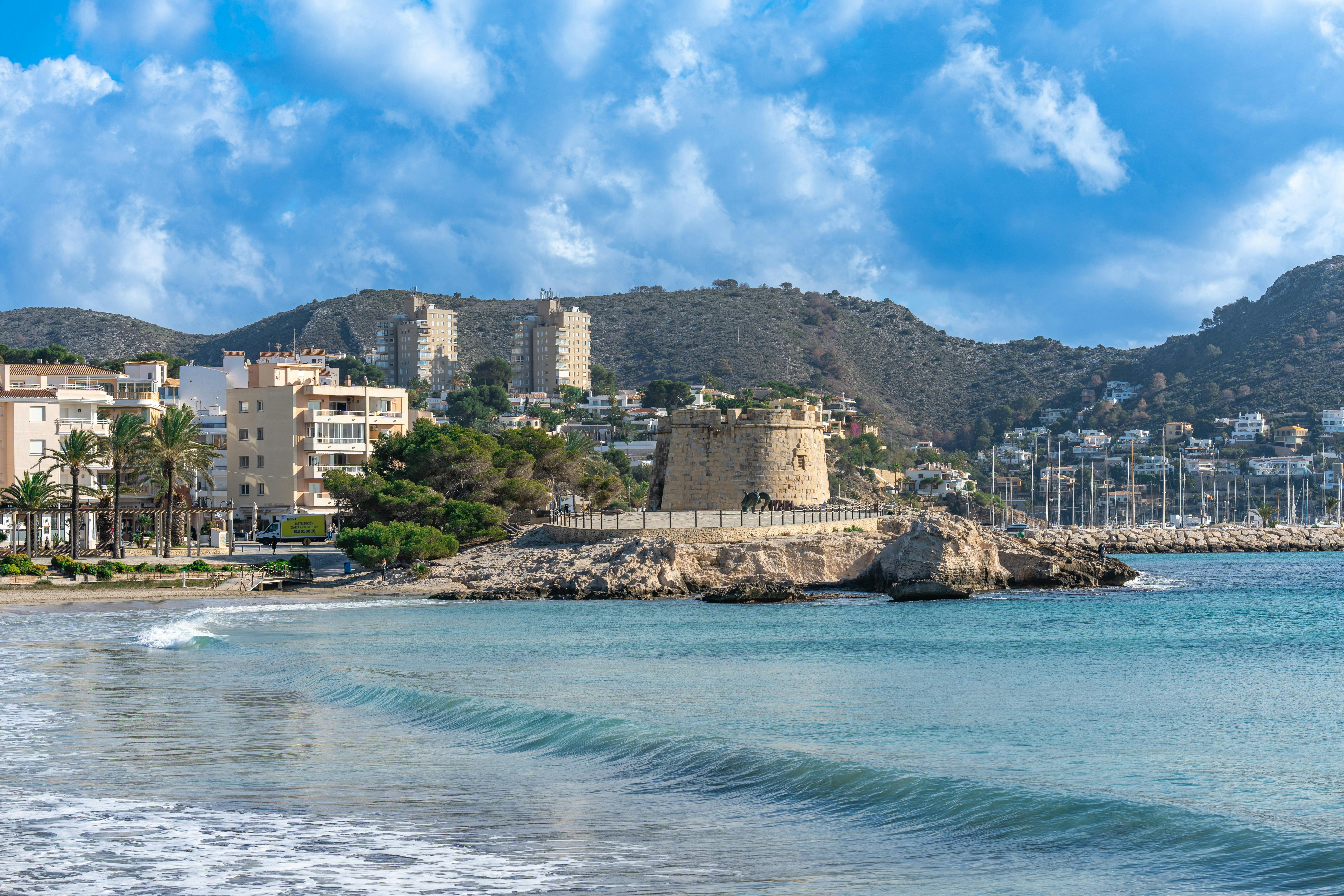 Beautiful coastal view of Moraira beach with historic tower and clear blue sky.